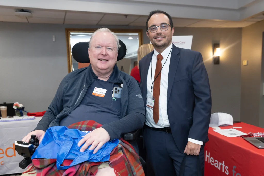 Photo of two individuals, one living with ALS, both looking forward and smiling